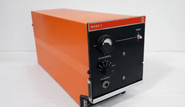 Orange metal test instrument with a black front panel, model 642C-1, featuring a large dial, channel knob, and headphones jack.