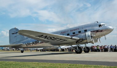 Silver vintage propeller airliner with ANSETT markings on the fuselage, taxiing on a runway as a crowd watches.