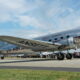 Silver vintage propeller airliner with ANSETT markings on the fuselage, taxiing on a runway as a crowd watches.