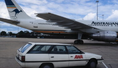 Large white airliner on the tarmac with a white sedan marked 'AWA' in the foreground.