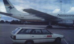 Airbus airliner at the airport with a kangaroo logo on the tail; a white AWA station wagon is parked in the foreground.