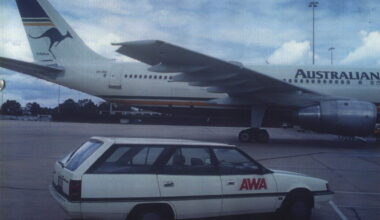Airbus airliner at the airport with a kangaroo logo on the tail; a white AWA station wagon is parked in the foreground.