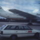 Airbus airliner at the airport with a kangaroo logo on the tail; a white AWA station wagon is parked in the foreground.